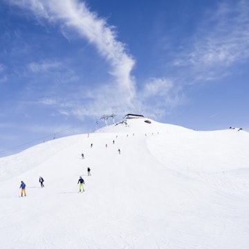 View from bottom of a ski hill of a bunch of skiers making their way down the hill, with a chair lift in the background